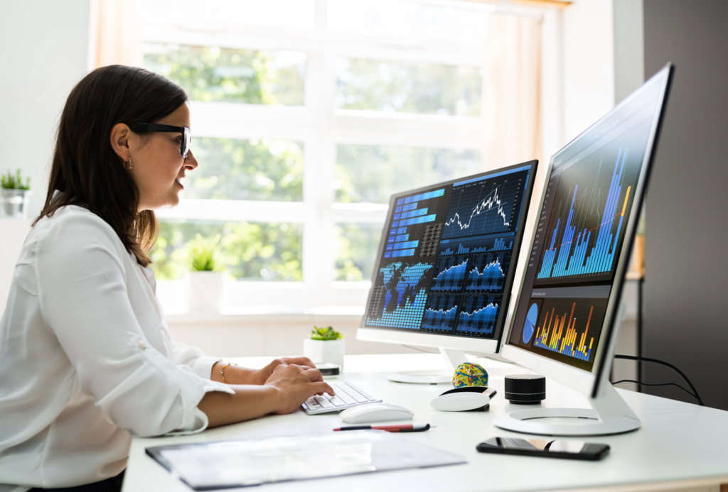 A person sits at a computer that has various charts and graphs displayed.